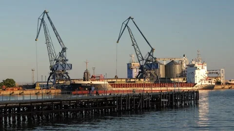 Industrial cranes loading grain onto a large cargo ship at the seaport Stock Footage 345004703