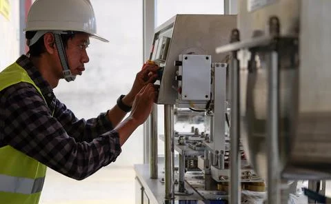 Industrial Engineer in hard hat is setting and checking process of machine in Stock Photos