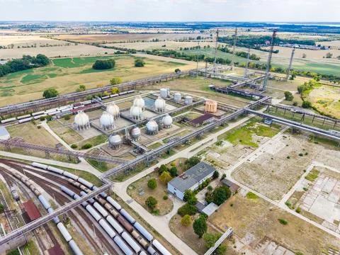 Industrial facility near fields with storage tanks and rail tracks during day Stock Photos