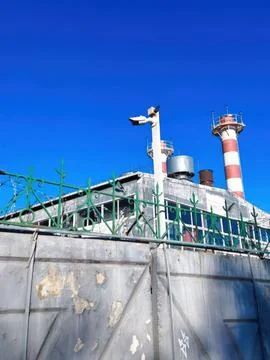Industrial facility with security camera and barbed wire fence under clear .. Foto stock