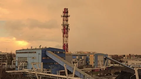 Industrial Facility with Smokestack Under a Dramatic Orange-Hued Sky at Sunset Видео 297356297