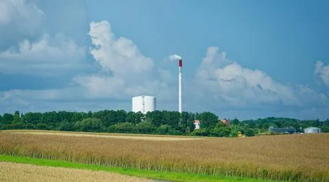 Industrial factory with smoke stack surrounded by green trees and golden fi.. 스톡 사진