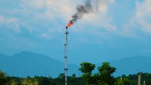 Industrial flare stack burning gas with smoke against a mountain backdrop 스톡 동영상 302571308