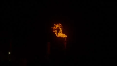An industrial flare stack burns off excess gas with a large, bright orange flame Stock Footage 322073710