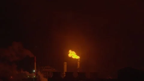 An industrial flare stack burns off excess gas with a large, bright orange flame Stock Footage 322073711