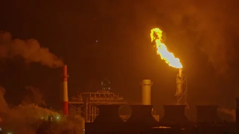 An industrial flare stack burns off excess gas with a large, bright orange flame Stock Footage 322073727