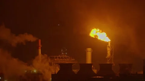 An industrial flare stack burns off excess gas with a large, bright orange flame Stock Footage 322073729