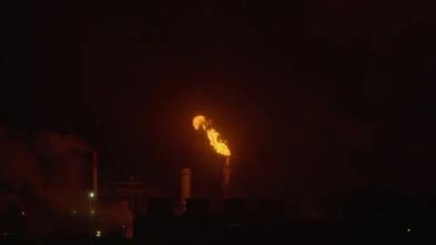 An industrial flare stack burns off excess gas with a large, bright orange flame Stock Footage 322073735