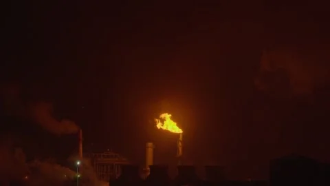 An industrial flare stack burns off excess gas with a large, bright orange flame Stock Footage 322073743