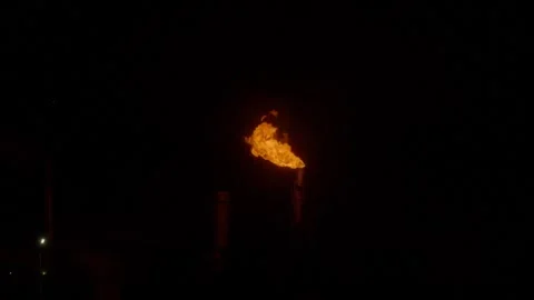 An industrial flare stack burns off excess gas with a large, bright orange flame Stock Footage 322073761
