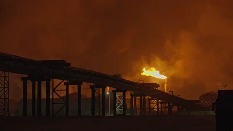 An industrial flare stack burns off excess gas with a large, bright orange flame Stock Footage 322073768