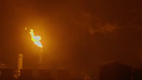 An industrial flare stack burns off excess gas with a large, bright orange flame Stock Footage 322073774