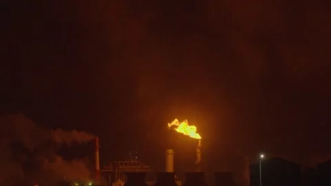 An industrial flare stack burns off excess gas with a large, bright orange flame Stock Footage 322073796