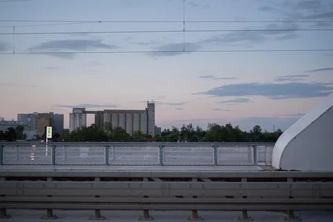Industrial grain silo complex stands behind trees and a transit platform Stock Photos
