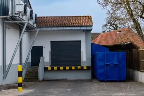 Industrial loading area with blue dumpster and storage door Stock Photos