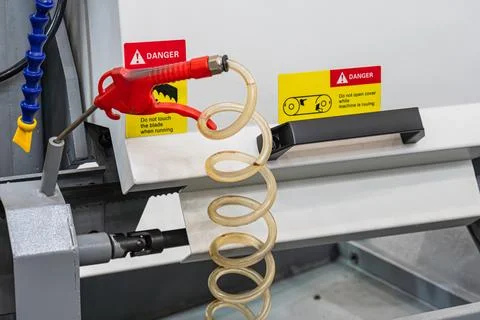 Industrial machine component featuring coiled translucent hose, red nozzle,.. Stock Photos