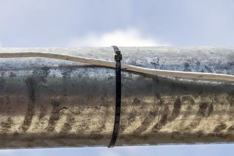 Industrial metallic pipe surface with cable secured using plastic zip tie Stock Photos