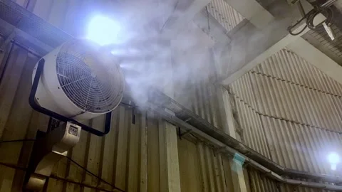 An industrial misting fan mounted on a wall, blowing a fine water mist to cool Stock Footage 346890389