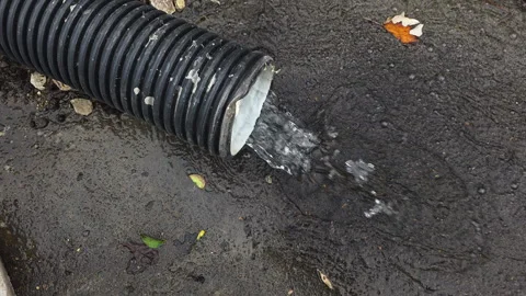 Industrial plastic pipe draining rainwater into a wet asphalt puddle during an Видео 329757548