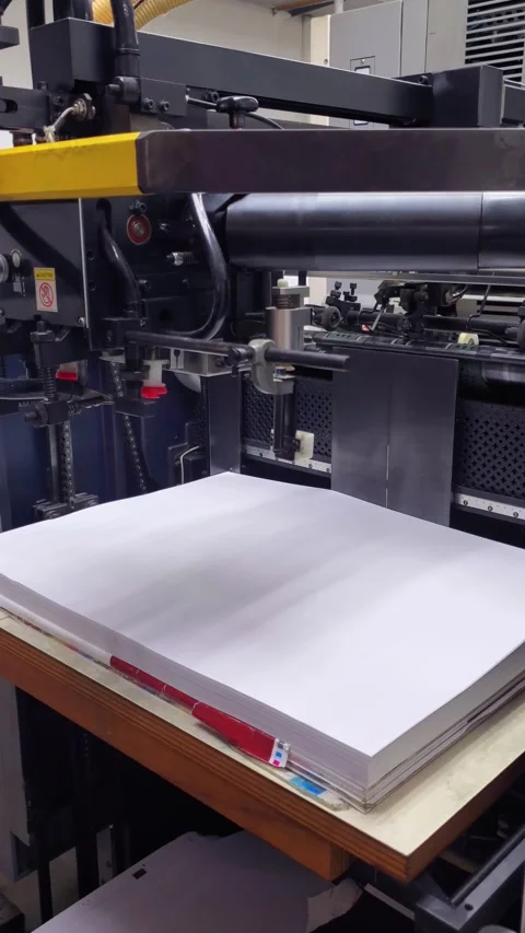 Industrial printing press operator manually aligning paper sheets for precise Stock Footage 338124500