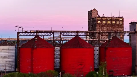 Industrial red grain elevator silos and plant at a vibrant pink sunset Stock Footage 340282247