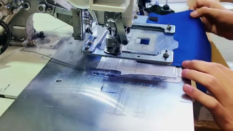 Industrial sewing machine guiding bright blue fabric on metal worktable while Stock Footage 346546038