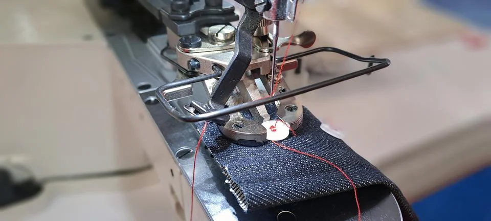 Industrial sewing machine stitching button on denim fabric Stock Photos