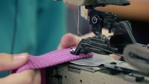 Industrial sewing machine stitching pink knit fabric. Close up hands factory. Stock Footage 345885256