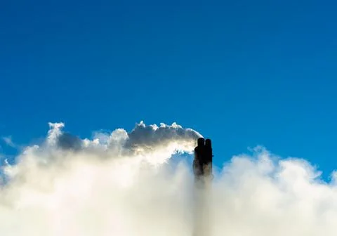 Industrial smoke stack putting out steam and smoke on a clear blue sky. Stock Photos