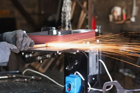 Industrial tool worker grinds a square steel pipe on a rotating belt sander Stock Photos