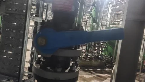 Industrial valve with a blue handle in a processing facility. Stock Photos