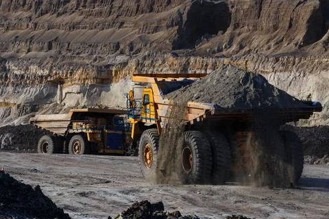 Industrial work in an open pit coal mine. A large yellow dump truck is carryi Stock Photos