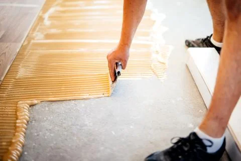 Industrial worker adding glue on cement floor, preparing surface for parquet Stock Photos