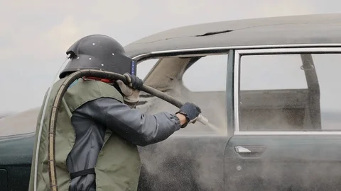 Industrial worker cleans metal surface of car by sandblaster gun Stock Footage 128263127