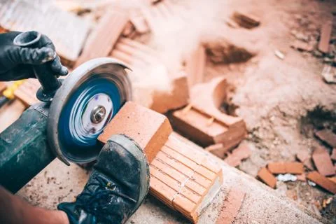 Industrial worker cutting through bricks. Professional brickmason using grind Stock Photos