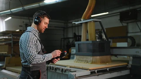Industrial worker with hearing protection operating a CNC cutting machine 動画素材 305604338