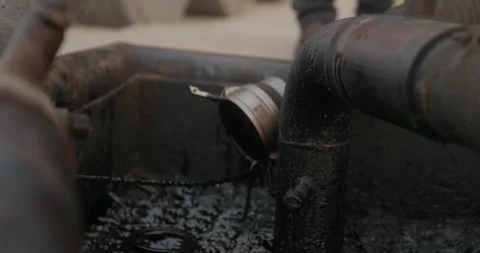 Industrial worker opens metal pipe valve above a tank filled with dark liquid 스톡 동영상 346315743