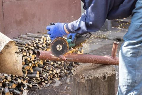 Industrial worker uses an electric angle grinder to cut a rusted metal pipe.. Stock Photos