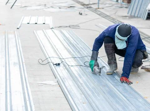 Industrial worker using an angle grinder to cut a metal sheet in a workshop. Stock Photos