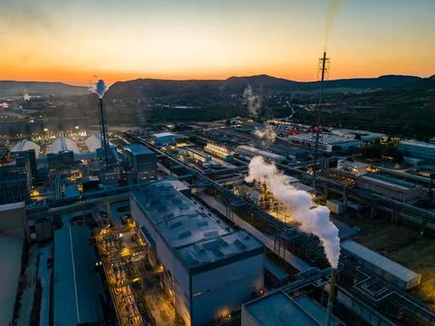 Industry facility with smoke stacks at sunset near hills and water Foto stock