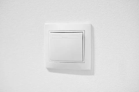 Inexpensive plastic push button switch against white wall. White common toggle Stock Photos