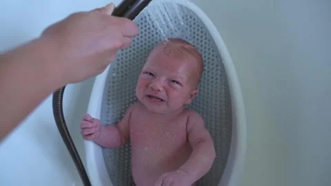 Infant bath scene, Child receiving soothing shower as parent gently rinses Stock Footage 325753709