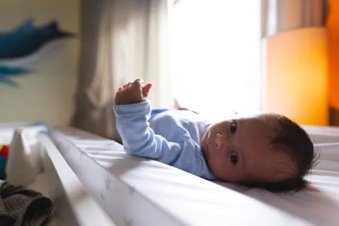 Infant boy lying on star-patterned changing pad at softly lit nursery, gazing Stock Photos