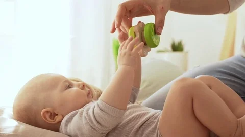 Infant caucasian baby boy lying on back while his mother playing with rattle toy Stock Footage