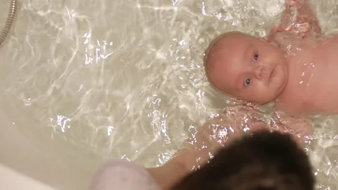 Infant child is bathing on his back floundering and supported by mother hands Stock Footage 136728464