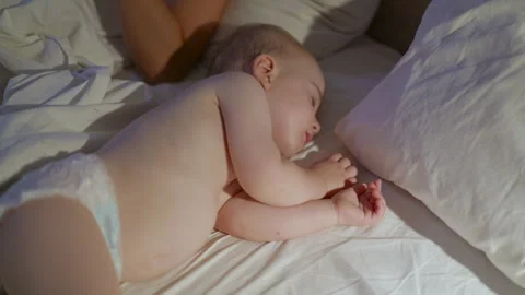 Infant child peacefully sleeping on a bed with white sheets and pillows, showing Stock Footage 341899502