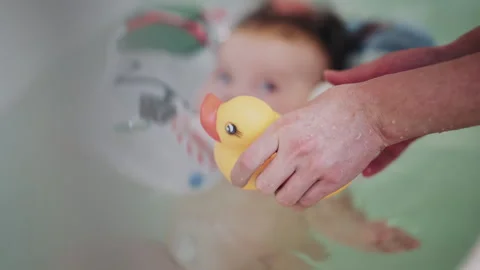 Infant floating in bathtub using inflatable baby bath support during bath time, Stock Footage 332539604