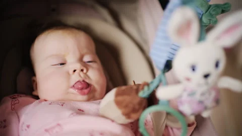 Infant lying on back under a soft baby play gym, looking up at hanging plush Stock Footage 329401006