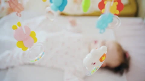 Infant lying in crib looking at colorful mobile toys hanging above 스톡 동영상 331027557