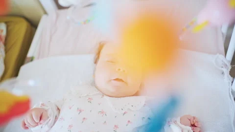 Infant lying in crib looking at colorful mobile toys hanging above 스톡 동영상 331027700